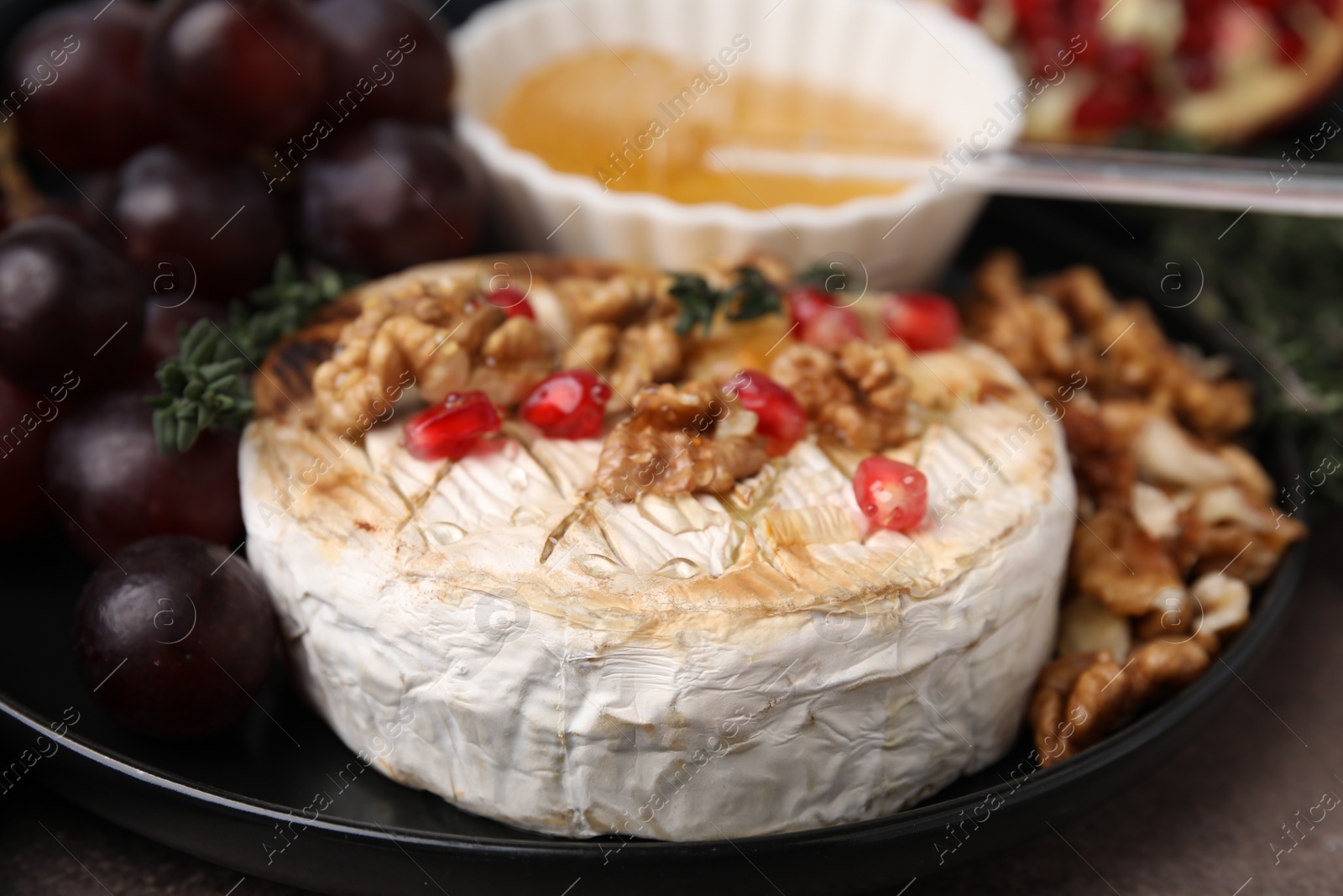 Photo of Plate with tasty baked camembert, honey, grapes, walnuts and pomegranate seeds on table, closeup
