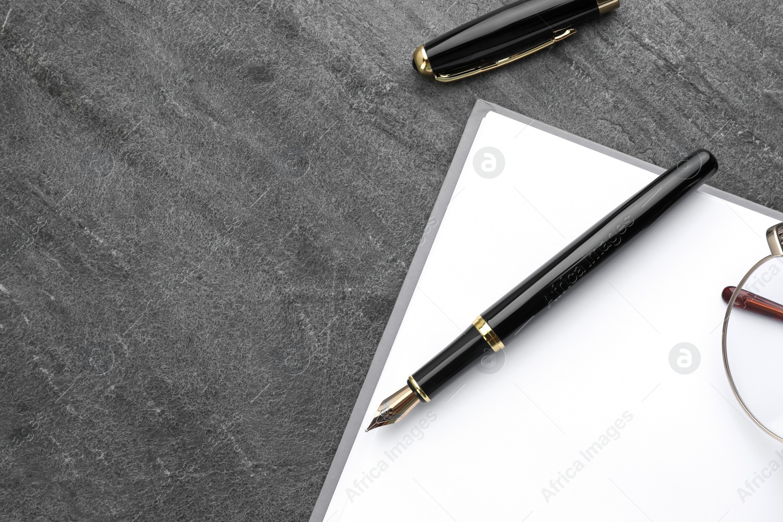 Photo of Stylish black fountain pen, open notebook and glasses on grey textured table, flat lay. Space for text