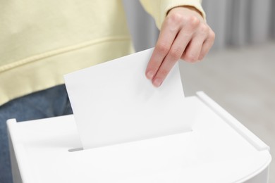 Photo of Woman putting her vote into ballot box on blurred background, closeup