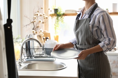 Photo of Woman with plate near sink in stylish kitchen, closeup