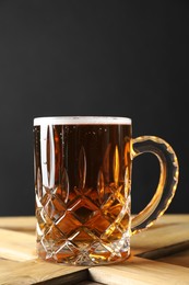Mug with fresh beer on wooden crate against dark grey background