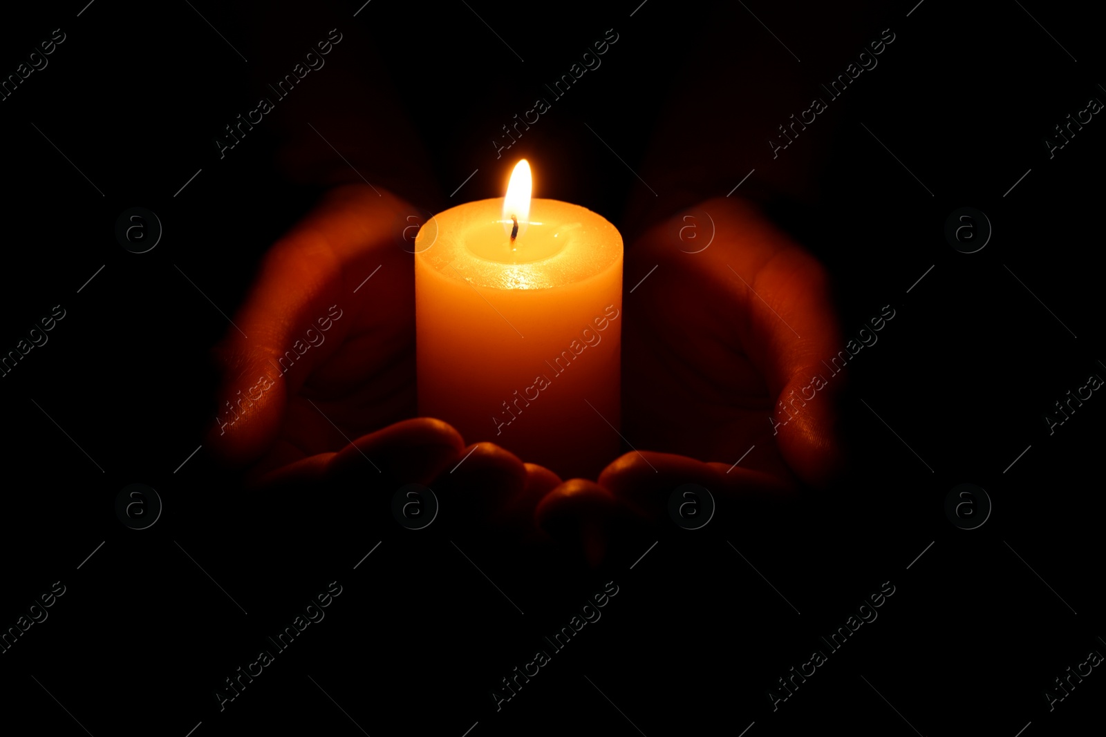 Photo of Woman holding burning candle in hands on black background, closeup