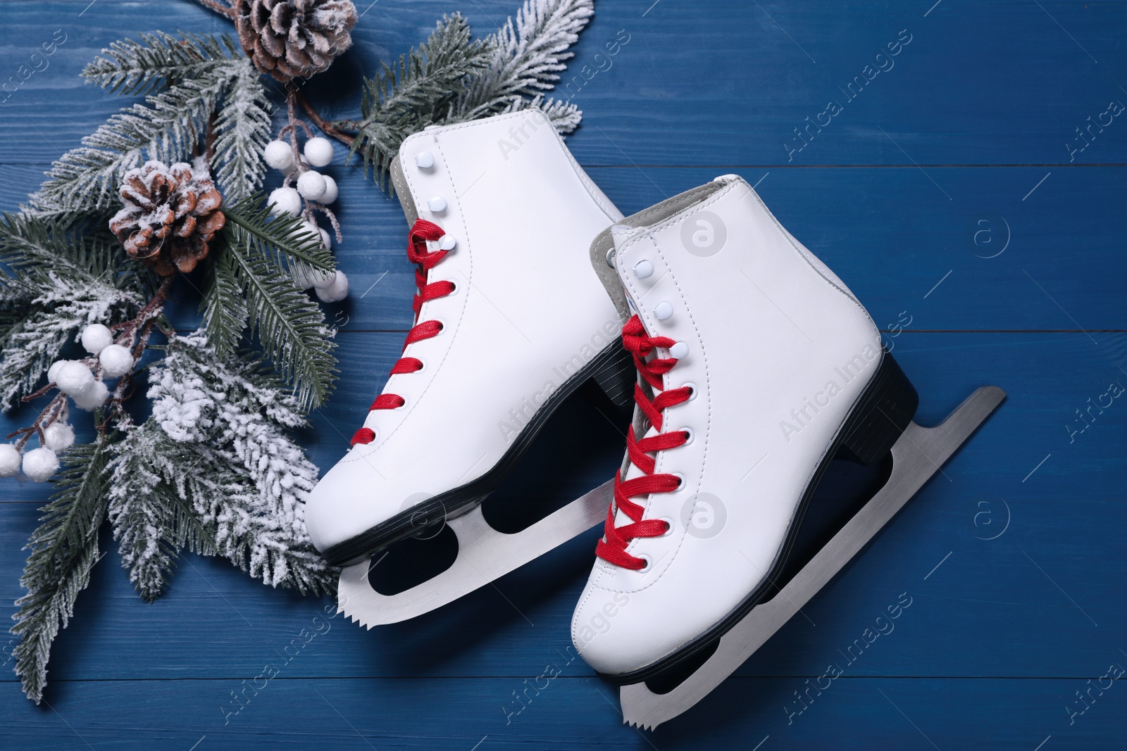 Photo of Pair of ice skates and beautiful Christmas decor on blue wooden table, flat lay