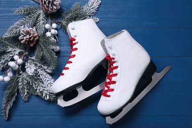 Pair of ice skates and beautiful Christmas decor on blue wooden table, flat lay