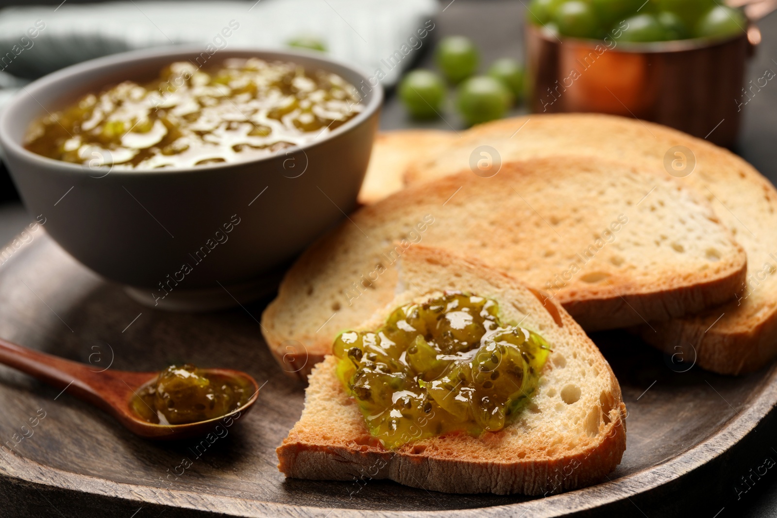 Photo of Toasts with delicious gooseberry jam on wooden plate, closeup