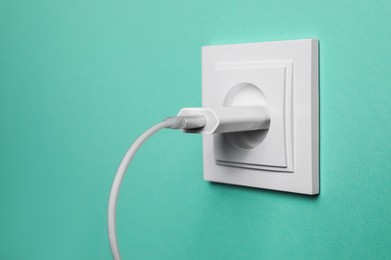 Photo of Power socket with inserted plug on turquoise wall, closeup. Electrical supply