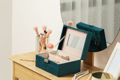 Photo of Jewelry box with many different accessories, perfume and makeup brushes on wooden table