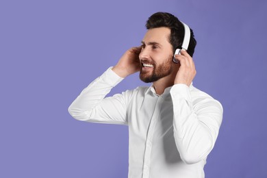Photo of Happy man listening music with headphones on violet background. Space for text