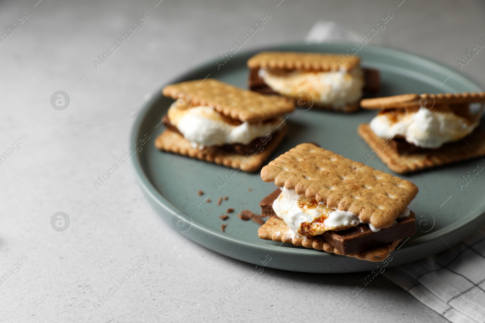 Photo of Delicious marshmallow sandwiches with crackers and chocolate on light grey table, closeup. Space for text