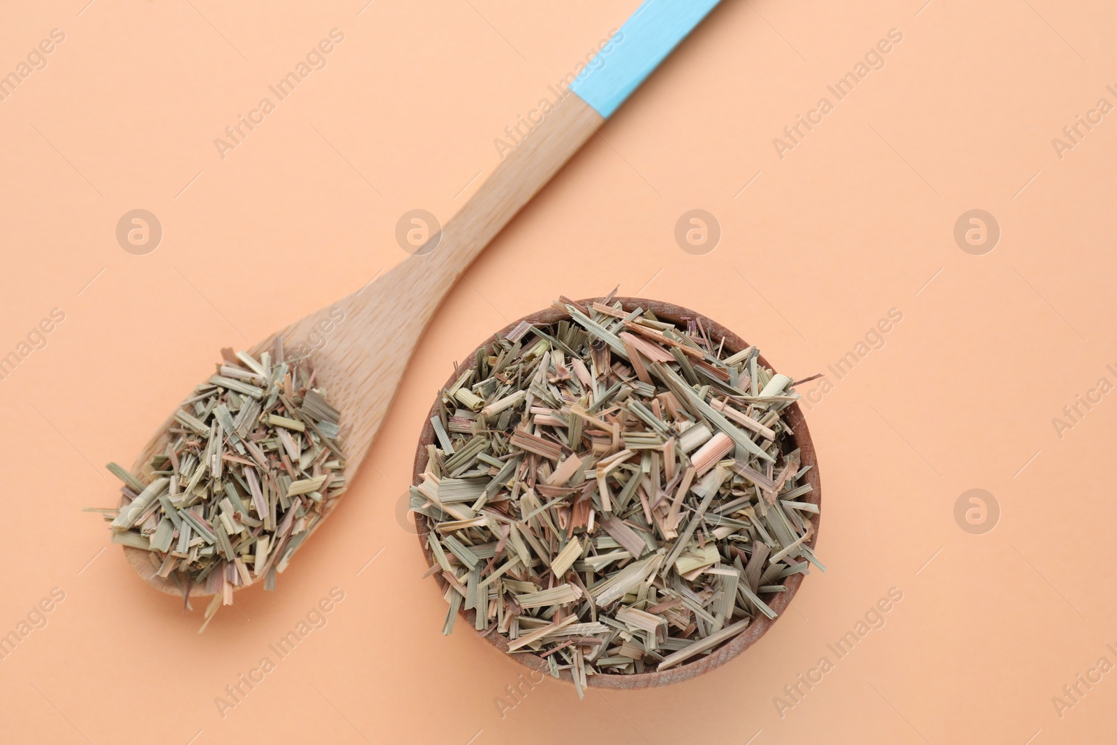 Photo of Wooden bowl and spoon with aromatic dried lemongrass on beige background, flat lay