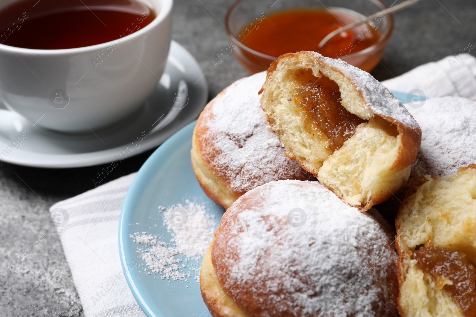 Photo of Delicious sweet buns with jam and cup of tea on table, closeup