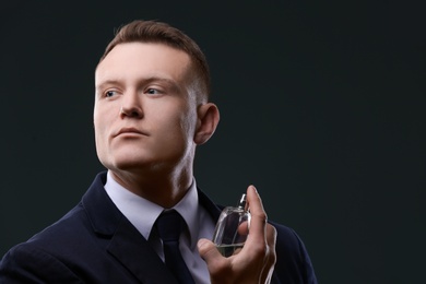 Photo of Handsome man in suit using perfume on dark background