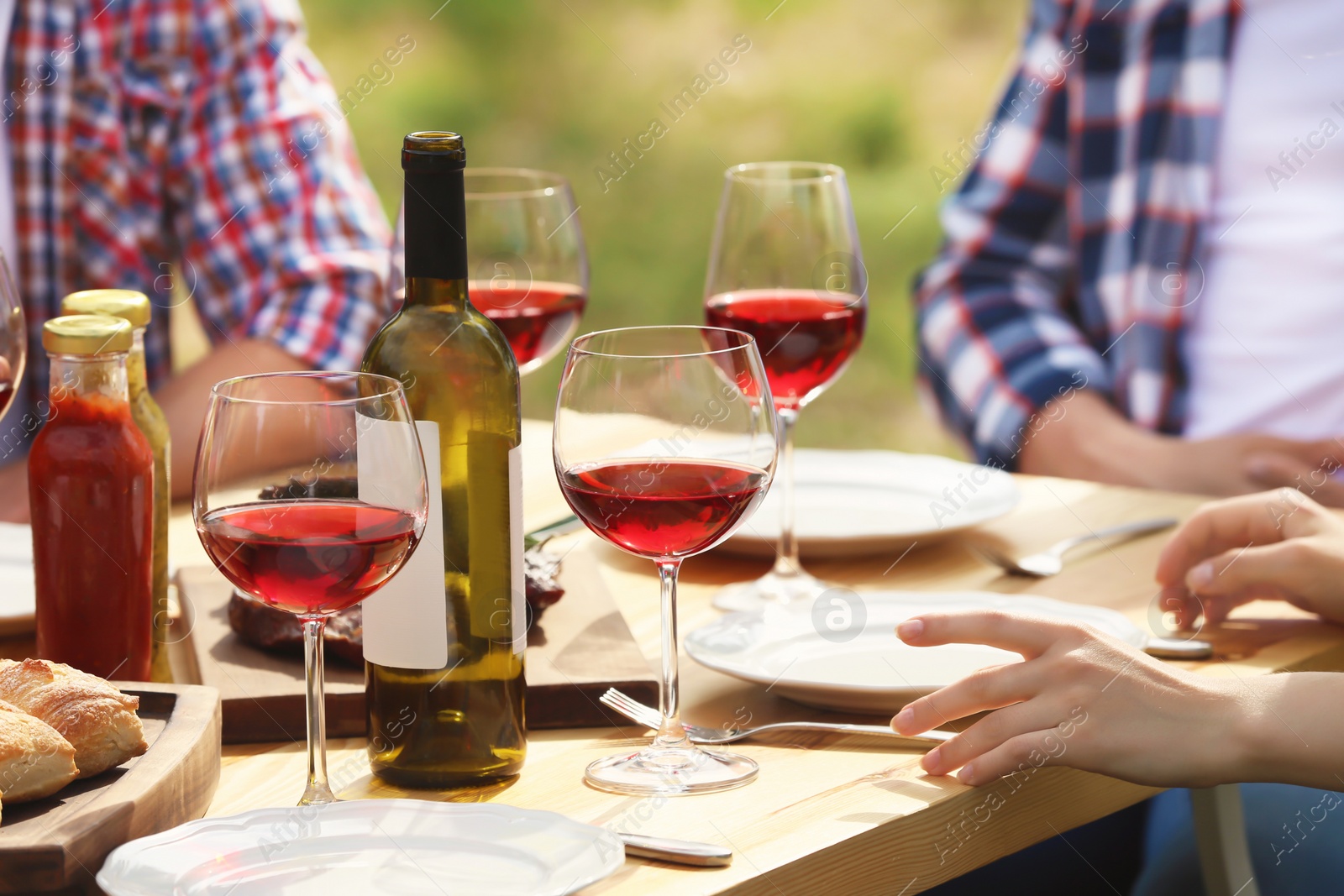 Photo of Young people with glasses of wine at table outdoors. Summer barbecue