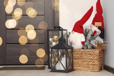 Photo of Christmas gnomes, lanterns with candles and balls near wooden door indoors