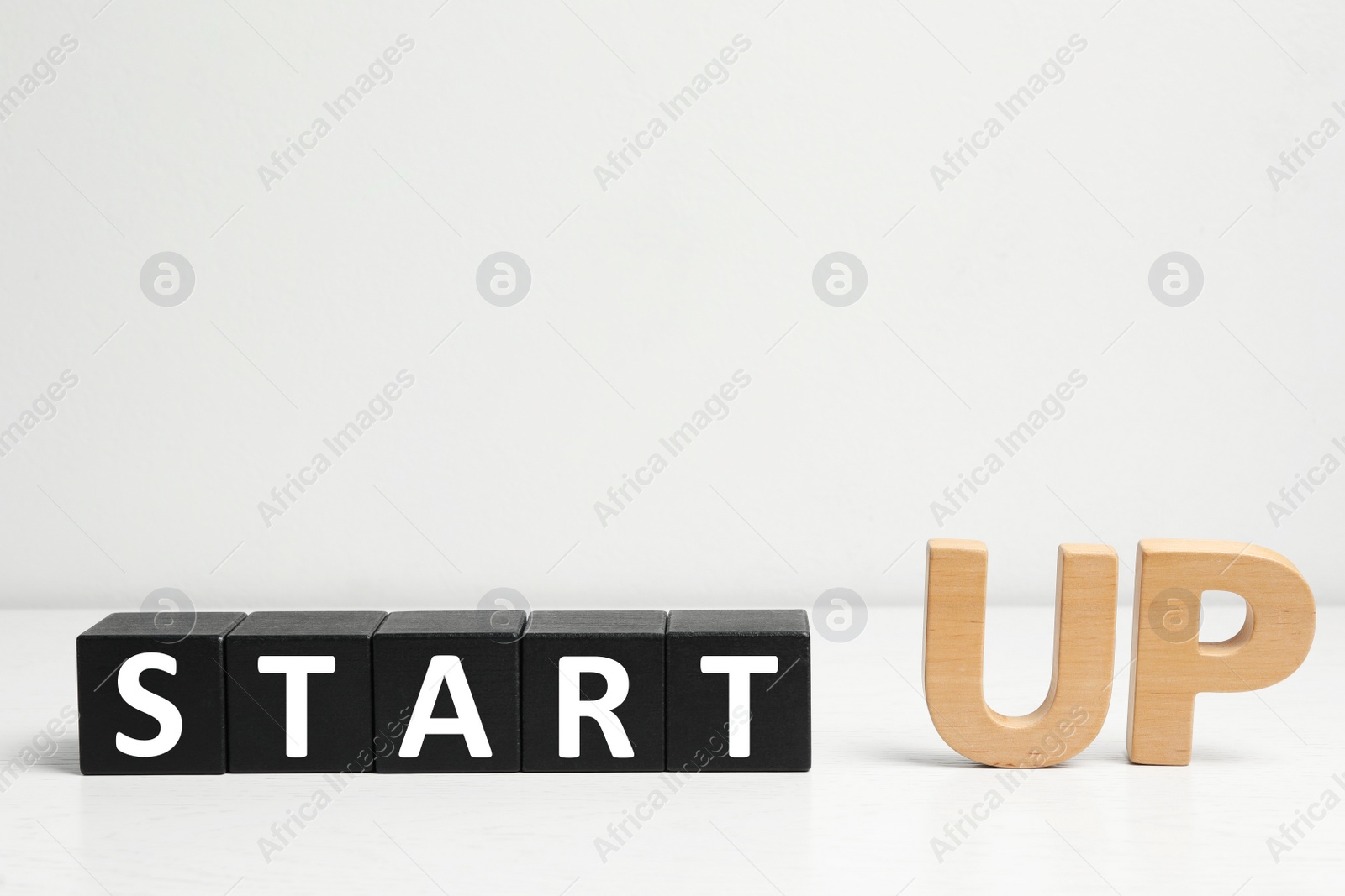 Photo of Words START UP made with black wooden blocks on white table