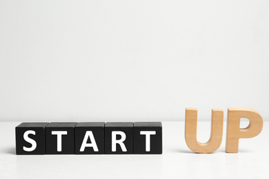 Words START UP made with black wooden blocks on white table