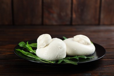 Photo of Delicious burrata cheese with arugula on wooden table, closeup