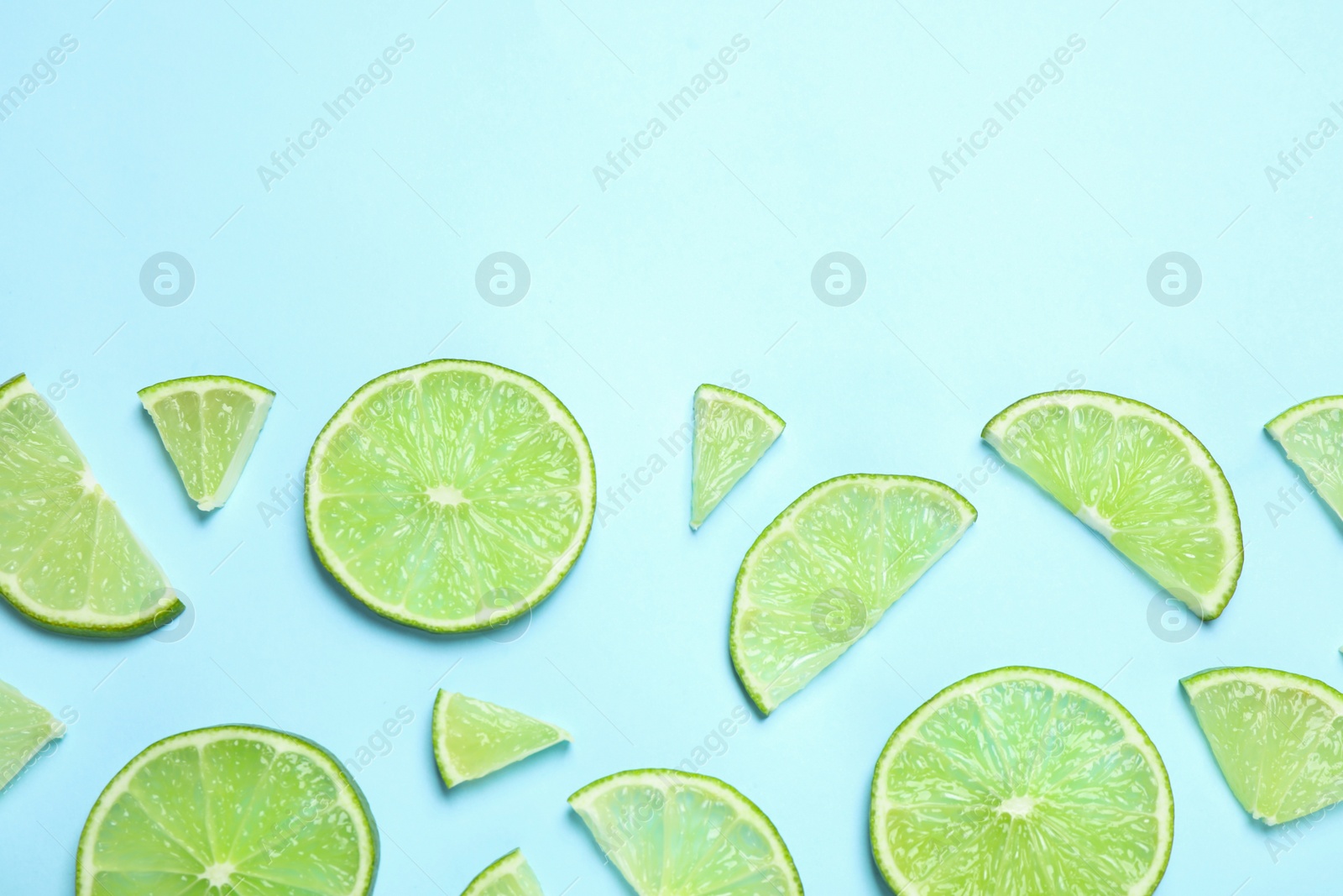 Photo of Juicy fresh lime slices on light blue background, flat lay. Space for text