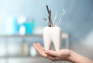 Dentist with tooth shaped holder full of professional tools in clinic, closeup