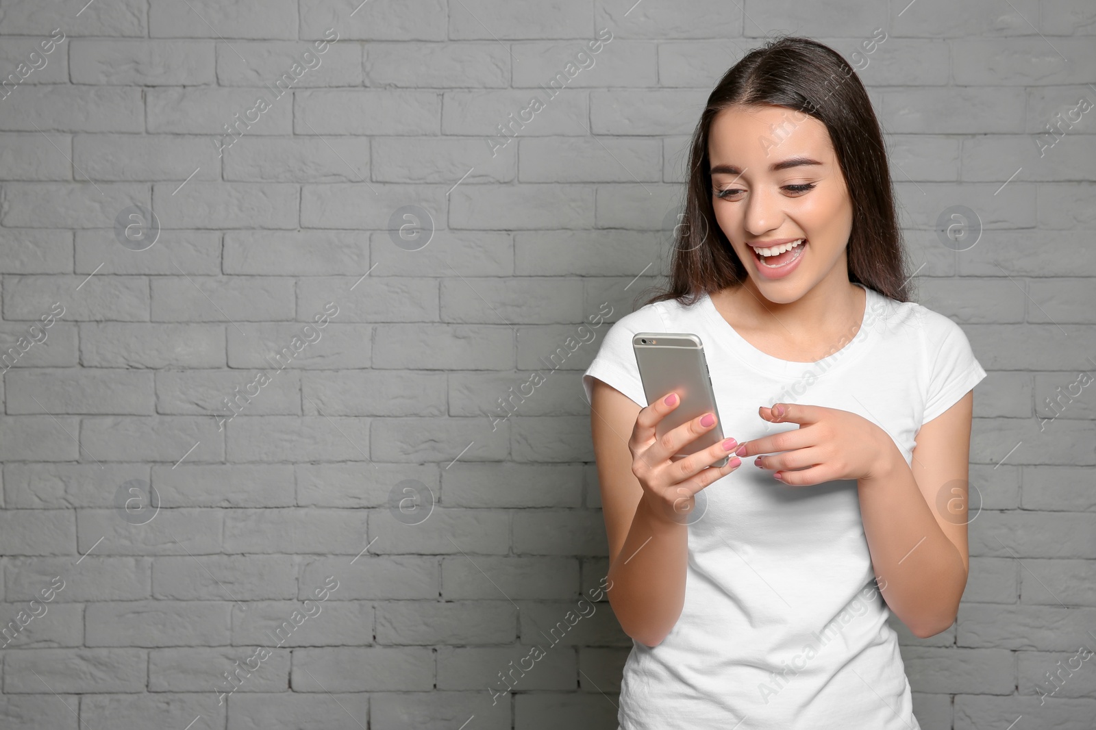 Photo of Attractive young woman using mobile phone on brick wall background