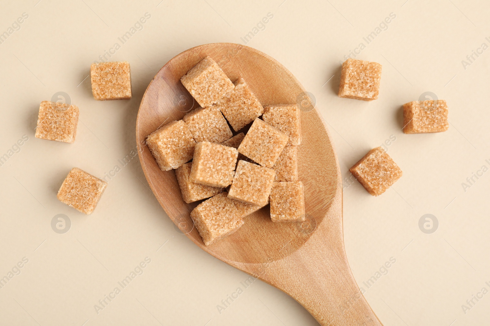 Photo of Brown sugar cubes in wooden spoon on beige background, top view