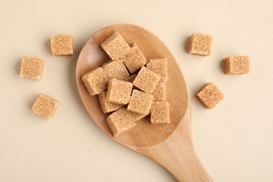 Photo of Brown sugar cubes in wooden spoon on beige background, top view