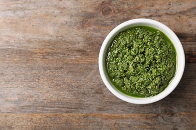 Photo of Homemade basil pesto sauce in bowl and space for text on wooden table