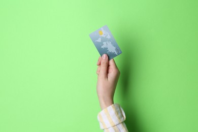 Photo of Woman holding credit card on light green background, closeup