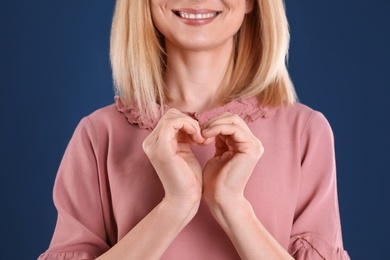 Photo of Woman making heart with her hands on color background, closeup