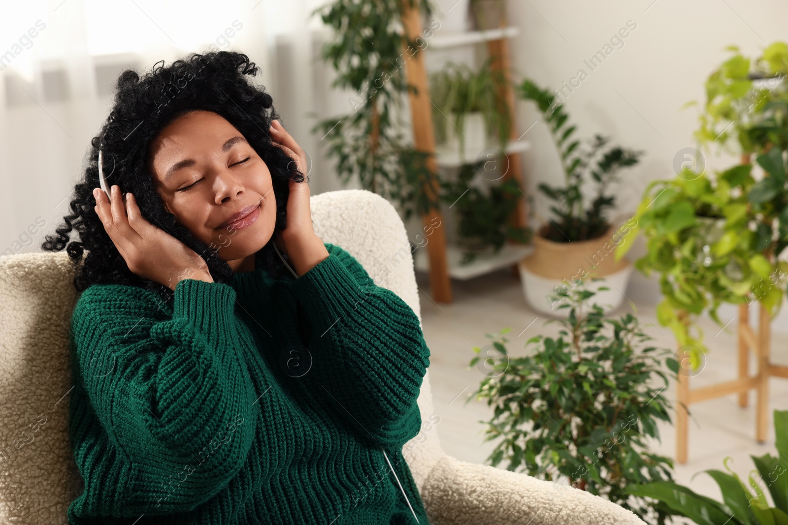 Photo of Relaxing atmosphere. Woman wearing headphones and listening music in room with beautiful houseplants. Space for text