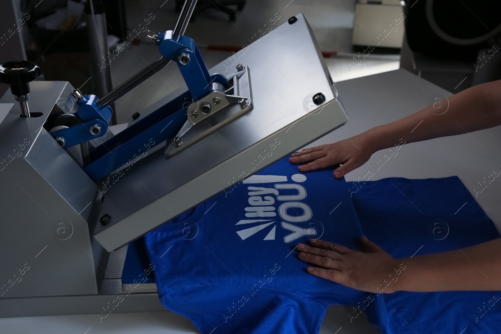 Photo of Printing logo. Woman with t-shirt using heat press at white table, closeup