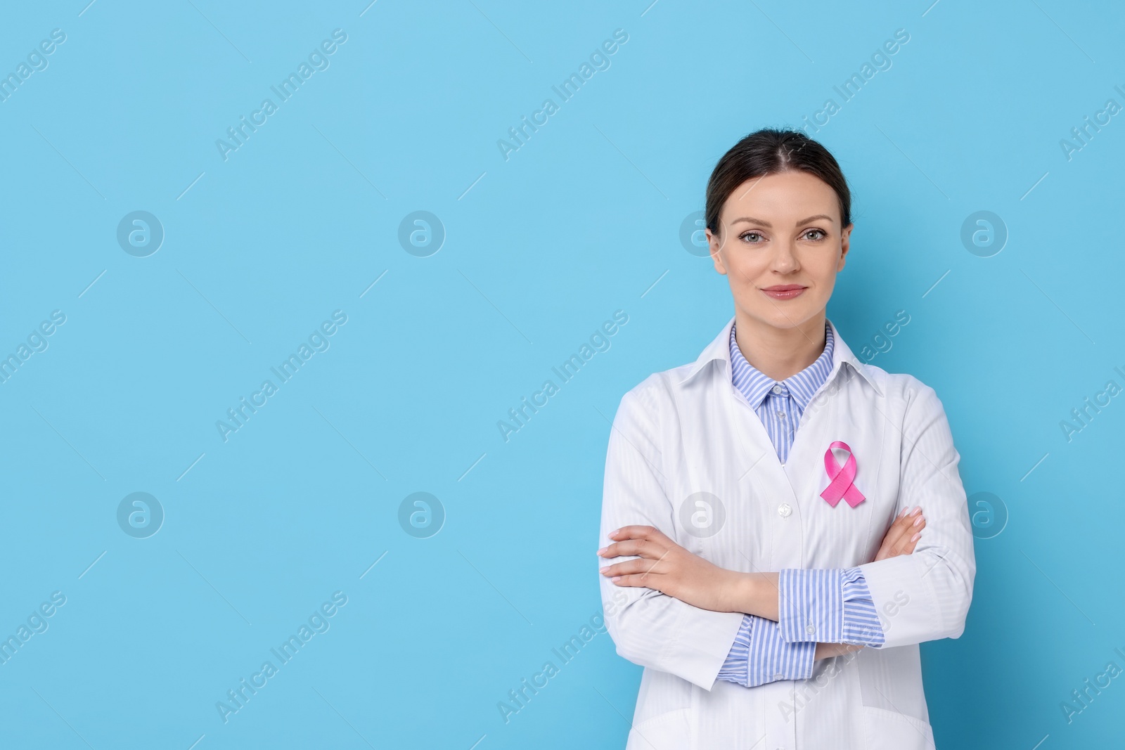 Photo of Mammologist with pink ribbon on light blue background, space for text. Breast cancer awareness