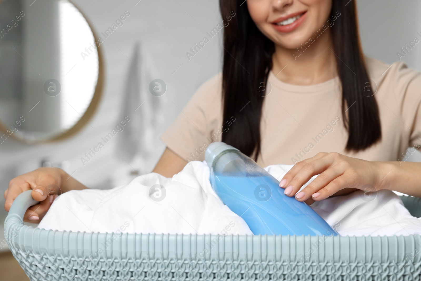 Photo of Woman holding basket with dirty clothes and fabric softener in bathroom, closeup