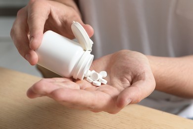 Man pouring pills from bottle at table, closeup