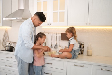 Photo of Little girls and their father cooking together in modern kitchen