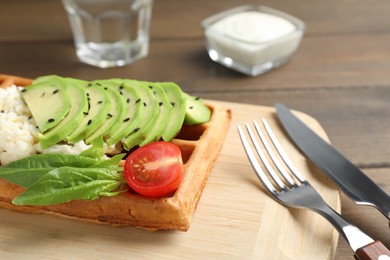 Photo of Fresh Belgian waffle with avocado, tomatoes and basil served for breakfast on wooden table, closeup