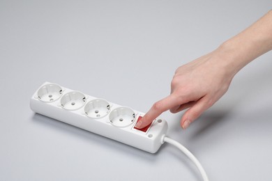 Woman pressing power button of extension cord on white background, closeup. Electrician's equipment