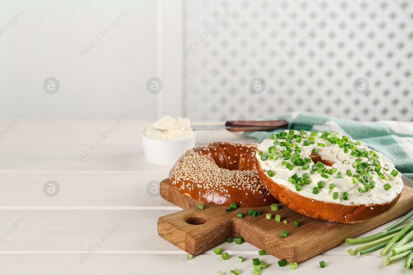 Photo of Delicious bagel with cream cheese and green onion on white wooden table. Space for text