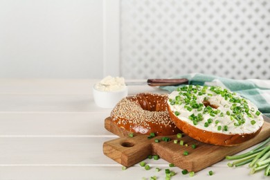 Delicious bagel with cream cheese and green onion on white wooden table. Space for text