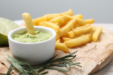 Photo of Delicious french fries, avocado dip, lime and rosemary on parchment