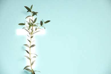 Photo of Shining cross and eucalyptus branch on turquoise background, space for text. Religion of Christianity