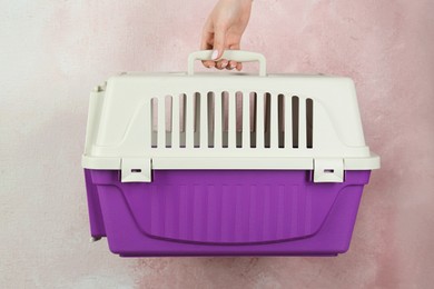 Woman holding violet pet carrier against pink wall, closeup