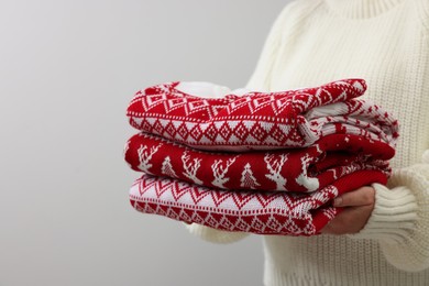 Photo of Woman holding stack of different Christmas sweaters on light grey background, closeup. Space for text