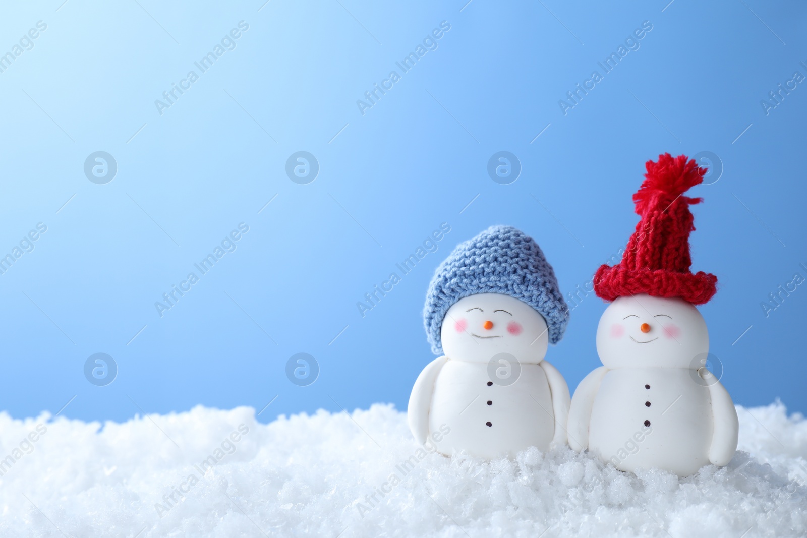 Photo of Cute decorative snowmen on artificial snow against light blue background, space for text