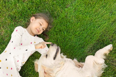 Photo of Cute little child with his pet on green grass, top view