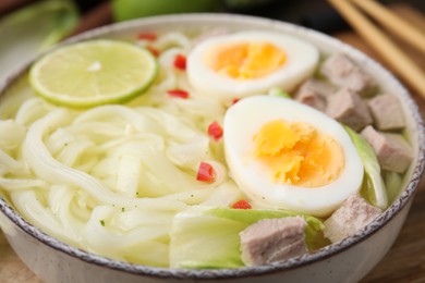 Photo of Bowl of delicious rice noodle soup with meat and egg on wooden board, closeup