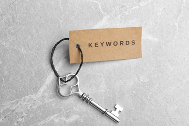 Photo of Vintage key and tag wIth word KEYWORDS on light grey table, top view