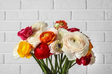 Photo of Beautiful spring ranunculus flowers against brick wall