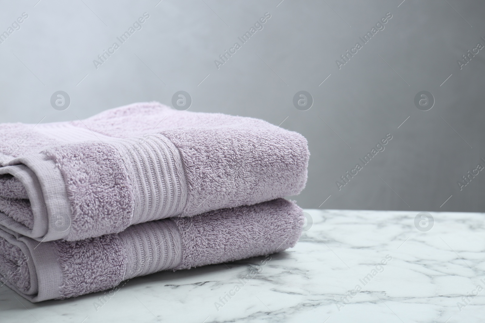 Photo of Folded violet terry towels on white marble table. Space for text