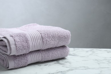 Folded violet terry towels on white marble table. Space for text